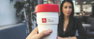 red and white to go mug made by Illy and a businesswoman in the background